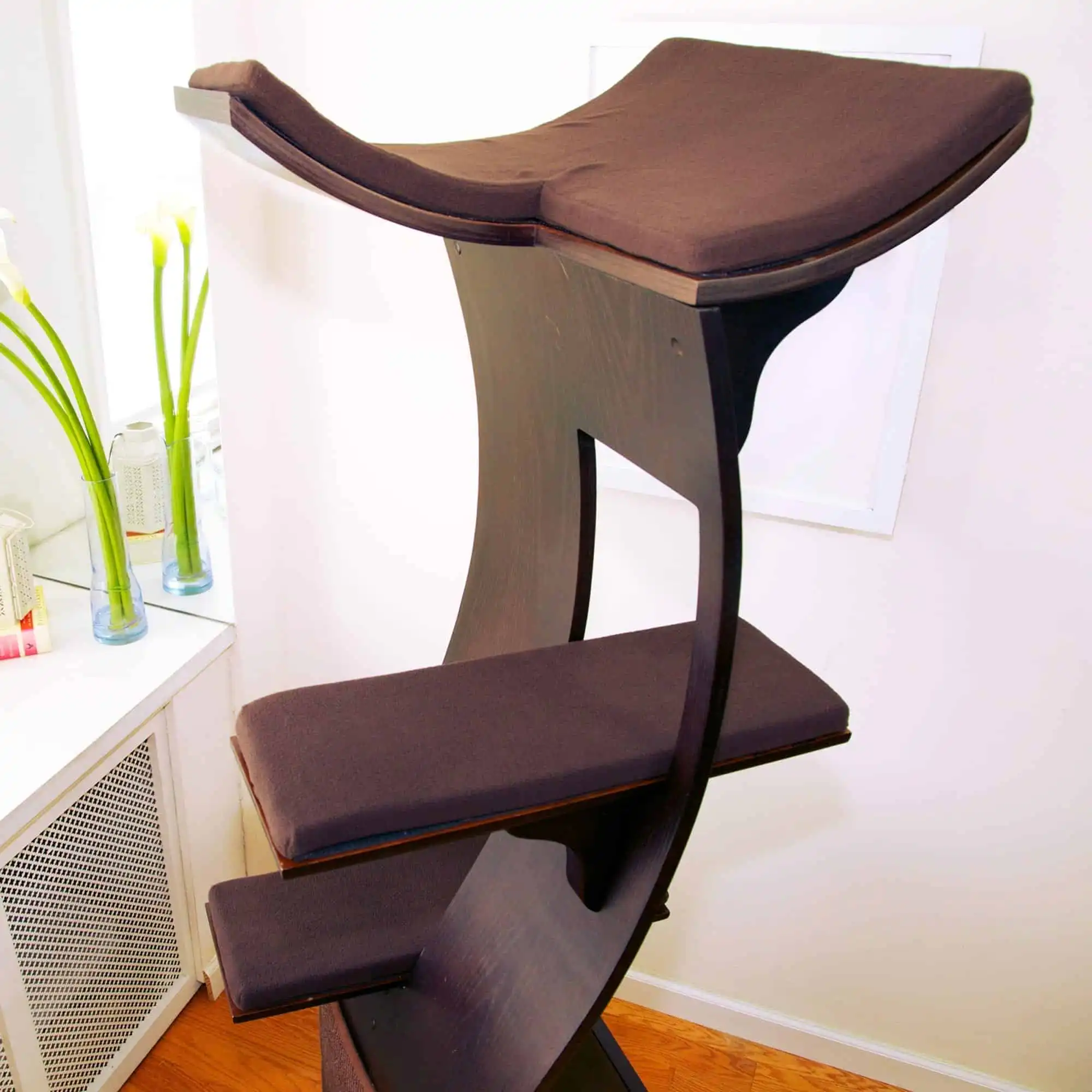 Brown Lotus Cat Tower with three cushioned platforms stands by a window in a bright corner next to flower vases.