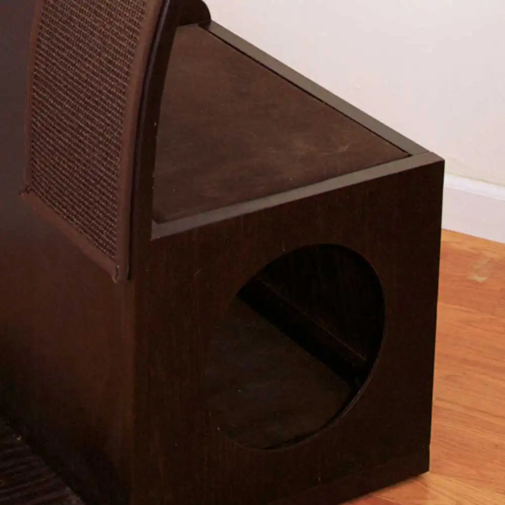 Dark wooden pet house with circular entrance, angled mesh panel, and cushion on hardwood floor by a white wall.
