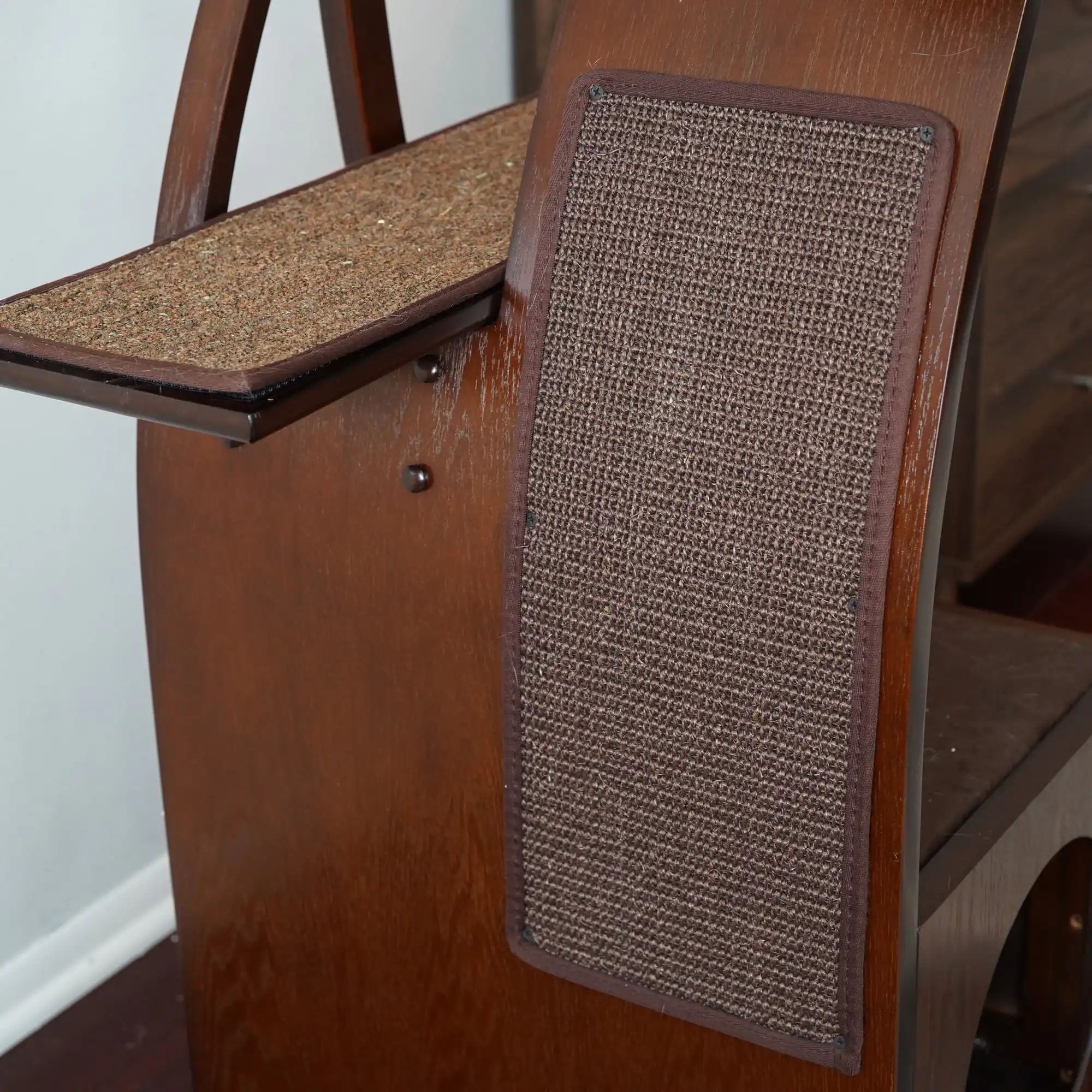 Wooden cat stand with side sisal scratch pad and carpeted top, placed indoors next to a wall.