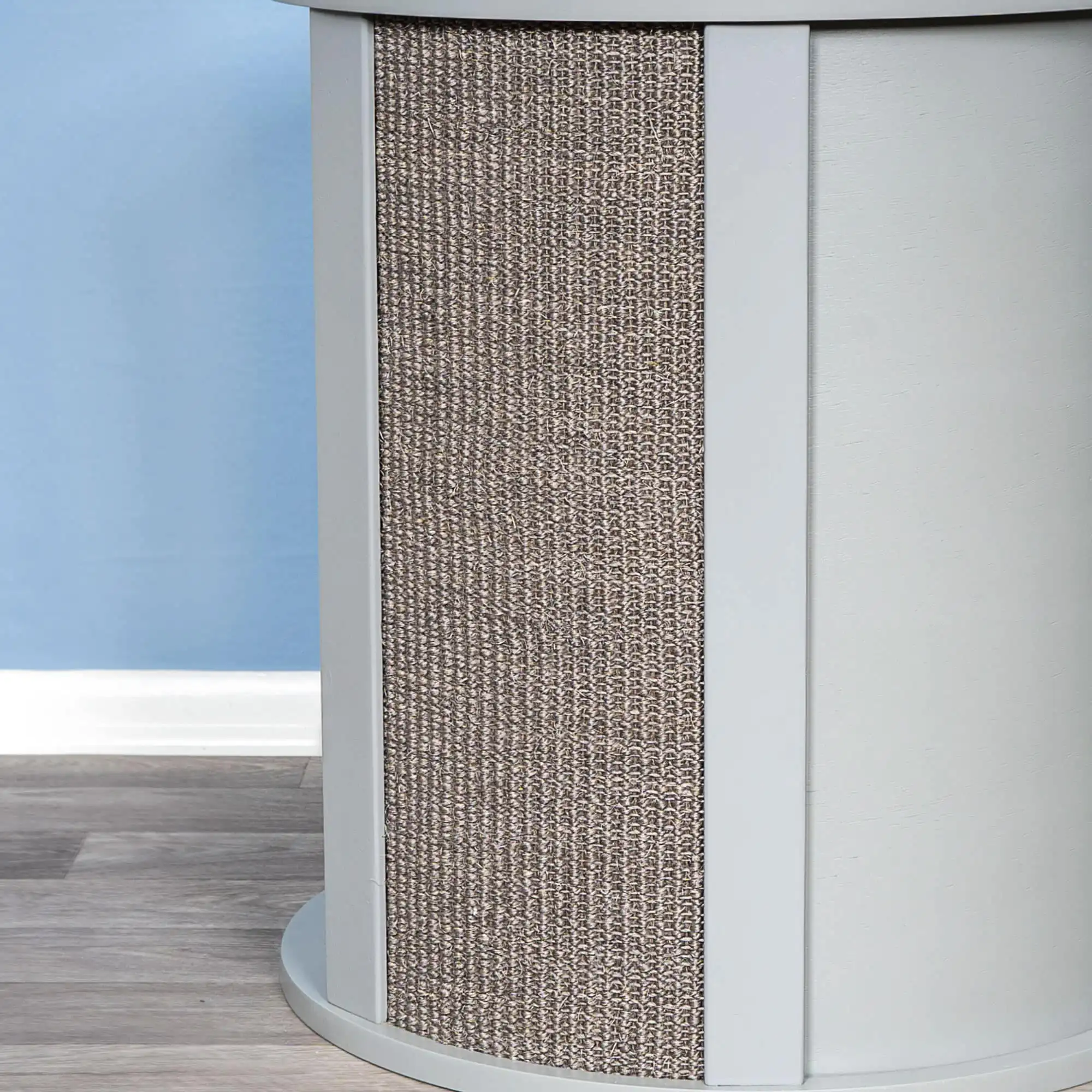 Close-up of a cylindrical light gray end table part with sisal texture, set before a blue wall and wood-patterned floor.