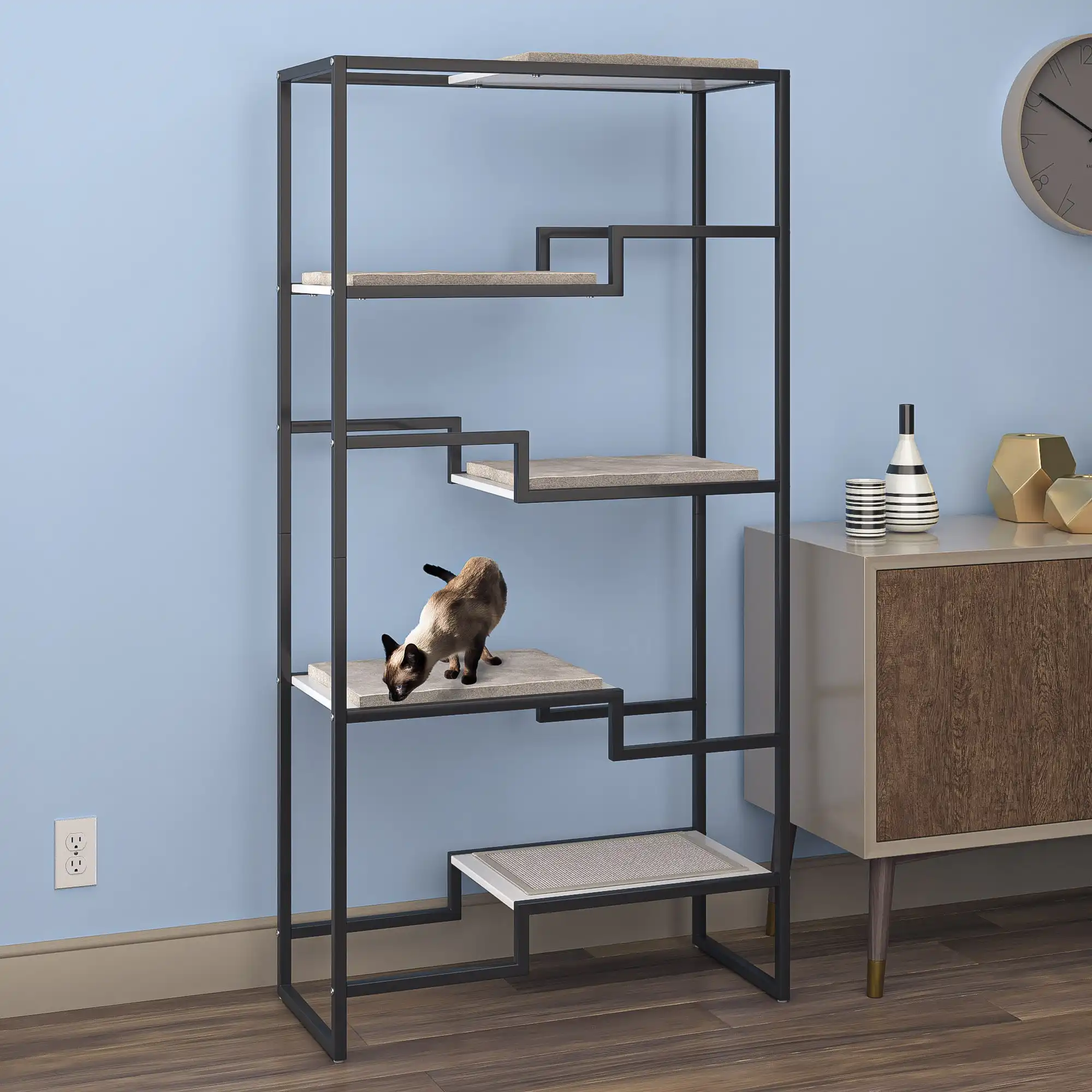 Siamese cat climbing a modern cat tree with black frame, white platforms, gray cushion, by a light blue living room wall.