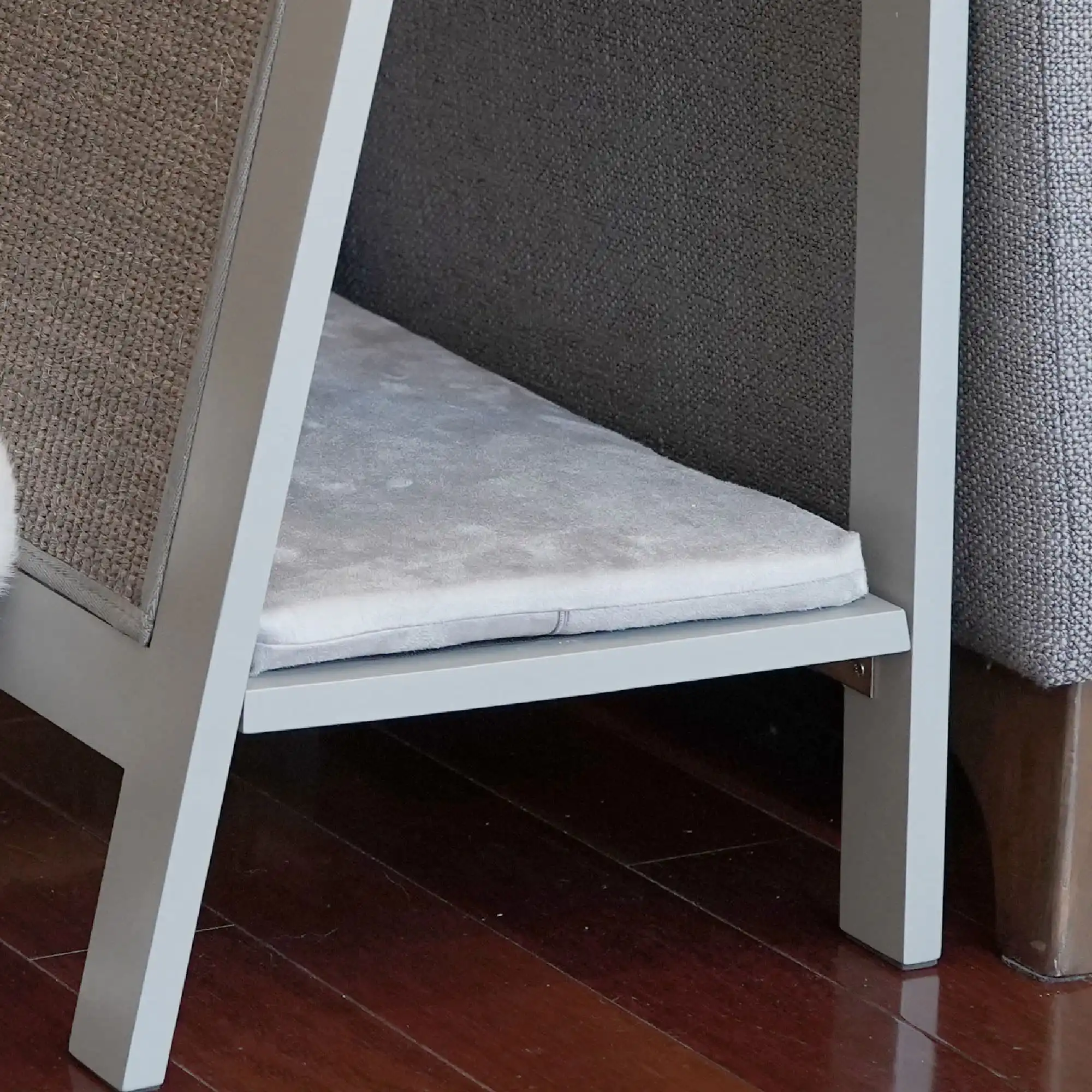 Small gray replacement cushion rests on a shelf under an A-Frame furniture piece with wooden legs on hardwood floor.