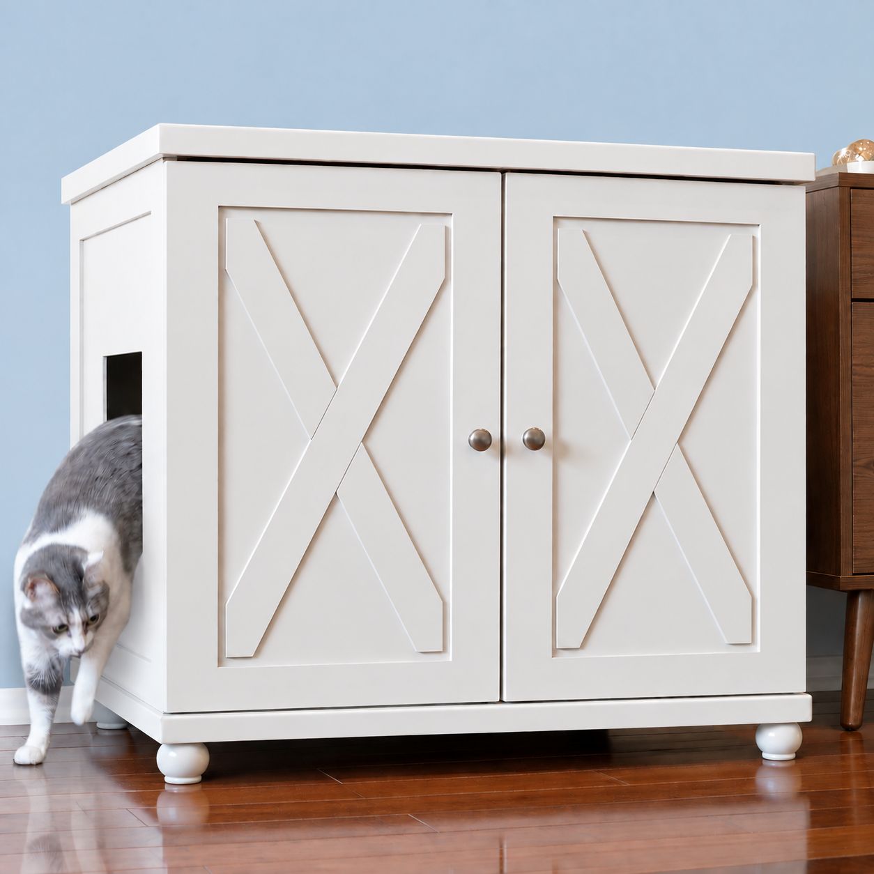 Grey and white cat stepping out of an ERLB-XL-WH-FARM-ROUND white wooden litter cabinet with an X-shaped design.