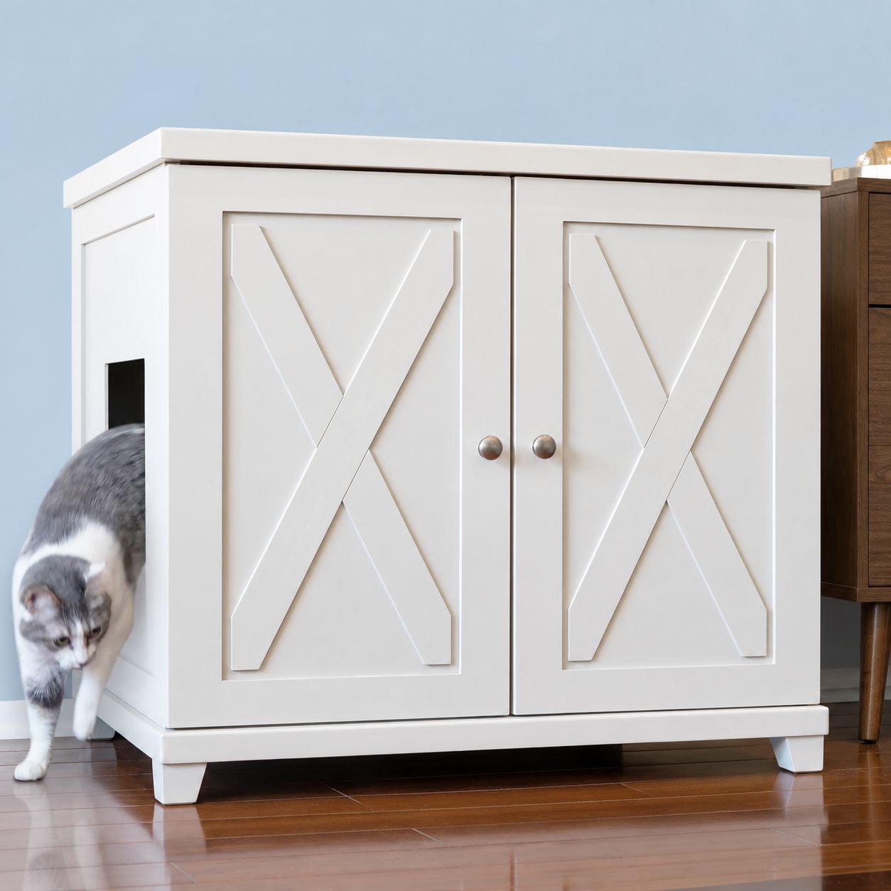A cat steps out of a white X-patterned ERLB-XL-WH-FARM-TAPE-CAT-LITTER-BOX-CABINET-FURNITURE with a side entrance.