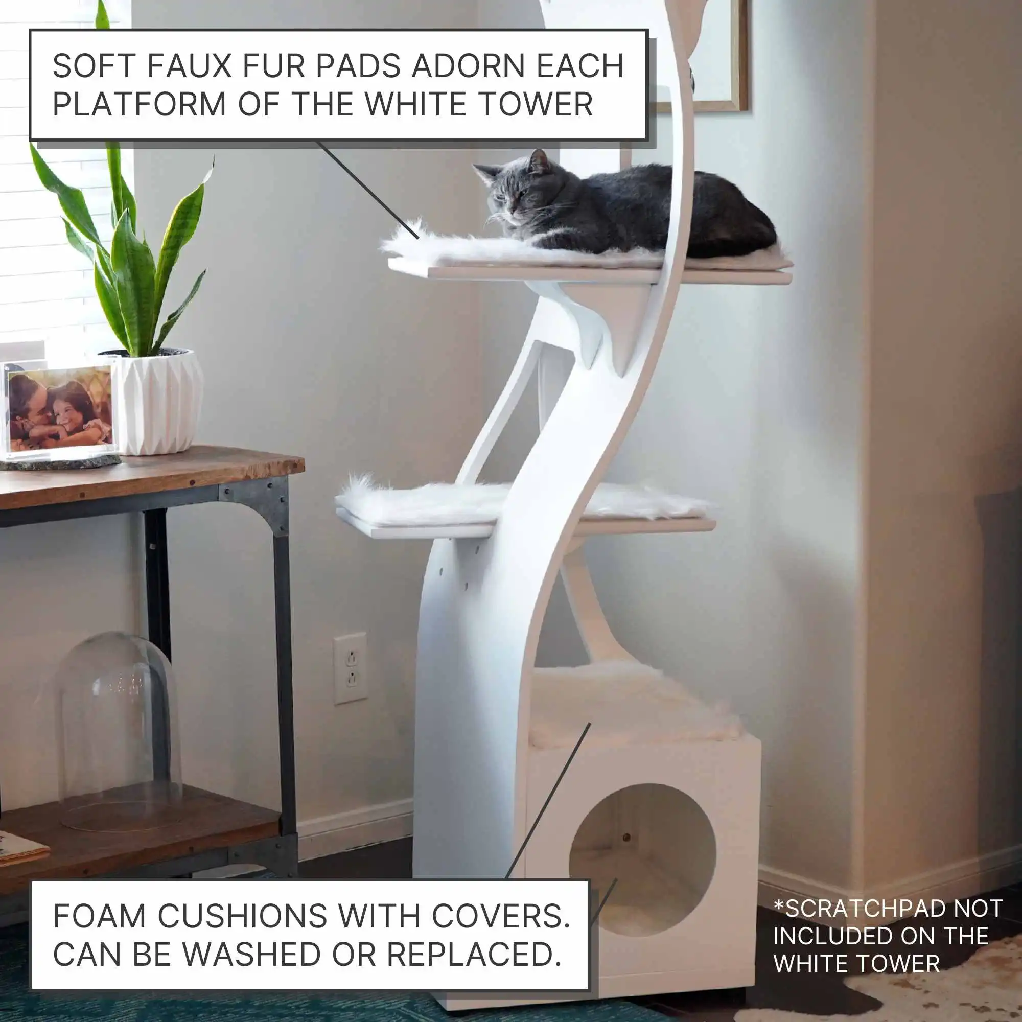 Gray cat resting atop Lotus cat tower with faux fur pads, next to a small table holding a plant and photo frame.