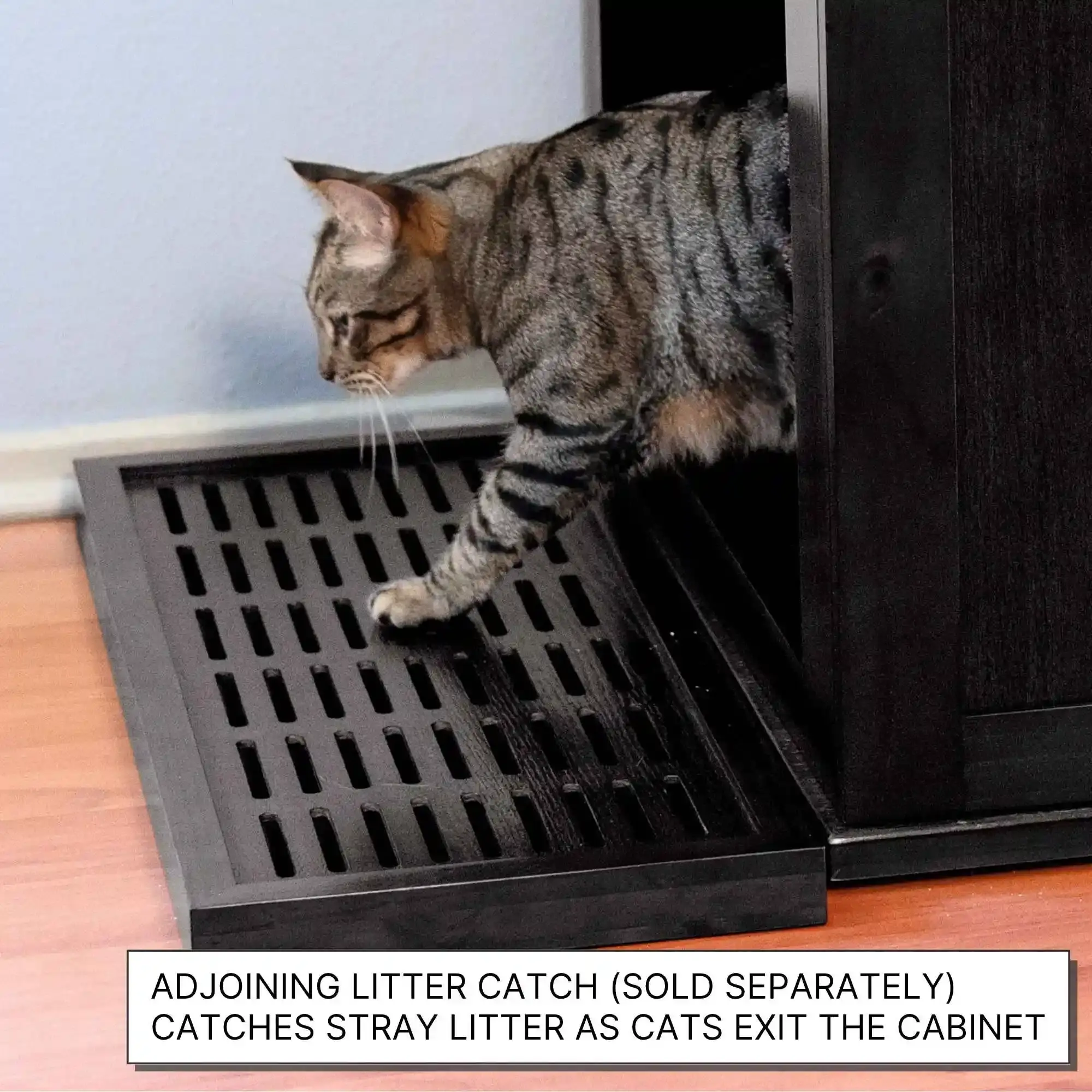Tabby cat stepping from a self-cleaning litter box onto a black grated mat, wood floor in the background.