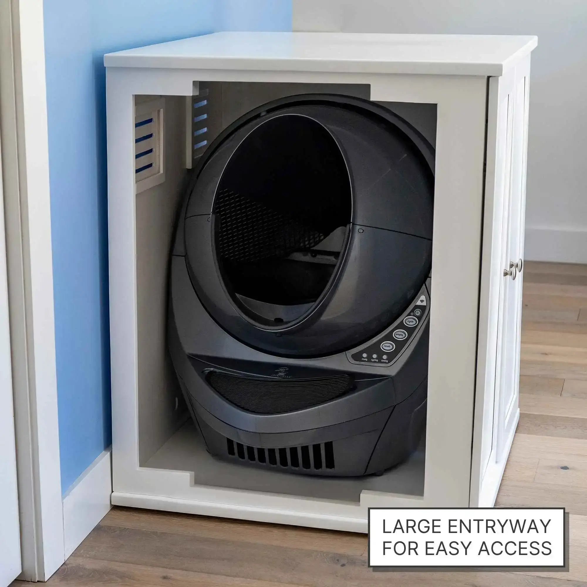 A black self-cleaning cat litter box sits inside a white cabinet with a large entryway and sign for easy access.