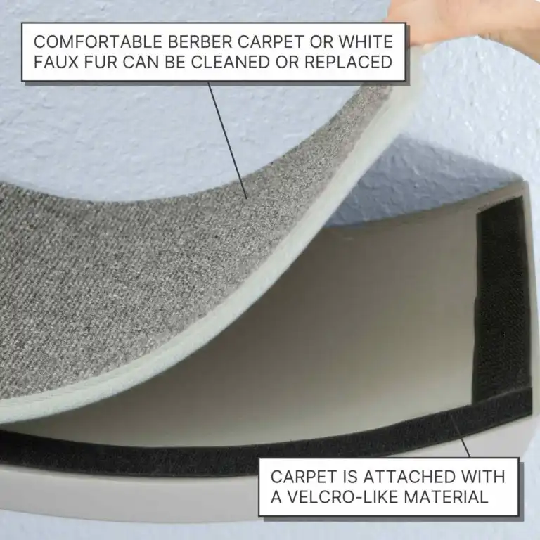 A hand lifts a gray carpet panel, attached by Velcro-like strips, from a wall-mounted wooden cat shelf.