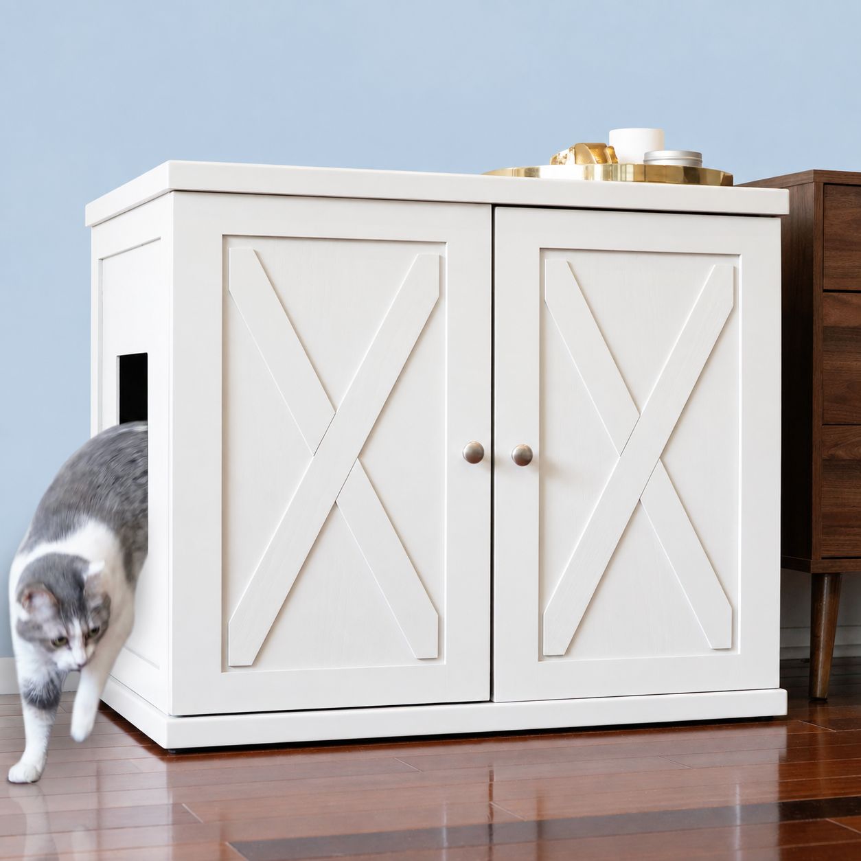 A grey and white tabby cat steps out of a White X-Panel Cat Cabinet.