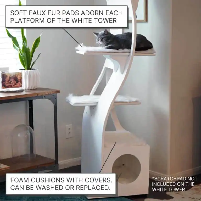 Gray cat resting on white modern cat tower with faux fur pads, near a potted plant, lamp, and decor.